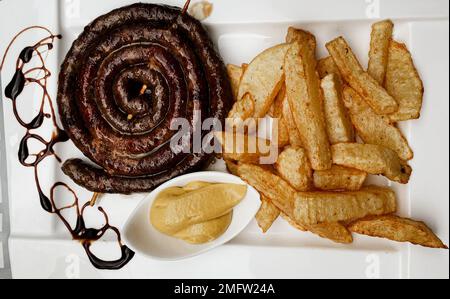 Nahaufnahme einer traditionellen spiralförmigen rumänischen Wurst, Pommes Frites und Senf auf einem Teller Stockfoto