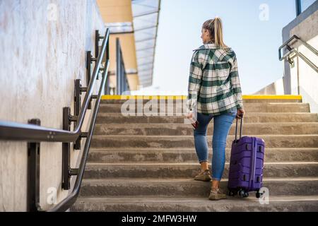 Frau mit Koffer und Ticket, die im Bahnhof über eine Treppe hinaufsteigt. Stockfoto