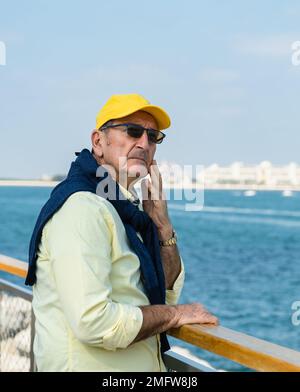 Ein älterer Mann, der an einer Promenade entlang an einem Yachthafen spaziert. Stockfoto
