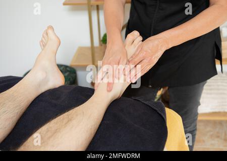 Weibliche Hände bei Wadenmassage an männlichen Beinen im Kosmetologie-Kursalon Stockfoto