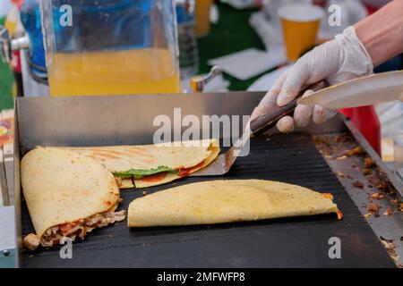 Der Koch bereitet frische Quesadilla auf dem schwarzen Grill auf dem Sommer-Markt vor Stockfoto