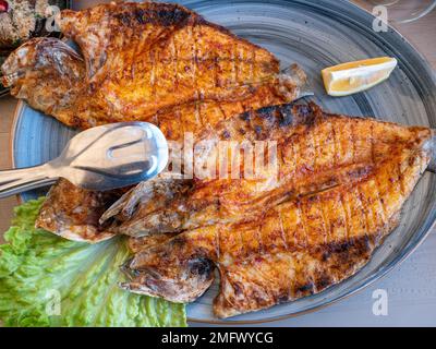 Gegrillter Fisch, gebratener Seebarsch auf dem Teller im Restaurant, gesunde Meeresfrüchte, Draufsicht. Stockfoto