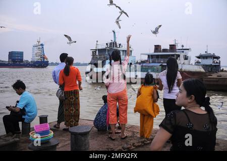 06.05.2014, Rangun (Yangon), Myanmar, Asien - Menschen füttern Möwen von einem Steg am Ufer des Yangon River (Hlaing River) mit Schiffen im Hintergrund. Stockfoto