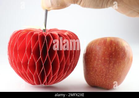 Origami-Apfel mit seinem Stiel in der Hand und echtem Apfel daneben, isoliert auf weißem Hintergrund Stockfoto