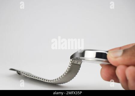 Uhr mit Armreifen aus Metall oder Edelstahl, die auf weißem Hintergrund in der Hand gehalten werden Stockfoto