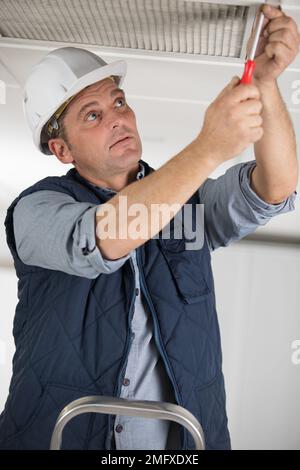 Professioneller Mann, der mit einem Schraubendreher an der Deckenentlüftung arbeitet Stockfoto