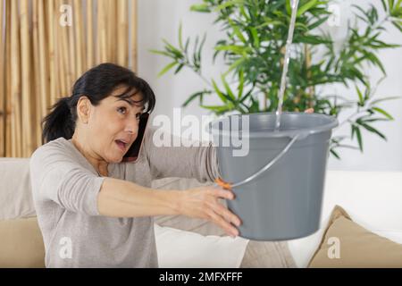 Schockierte Frau, die den Klempner anrief, als sie Wasser sammelte Stockfoto