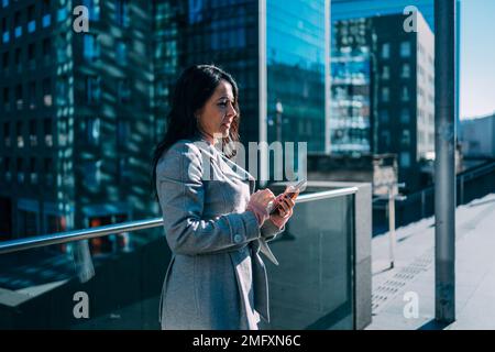 Glückliche brünette Frau, die im Business Center auf das Handy schaut Stockfoto