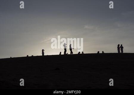 Hinterleuchtete Silhouetten von Menschen auf den roten Sanddünen in Mui Ne Vietnam mit Sonnenuntergang oder Sonnenaufgang dahinter. Stockfoto