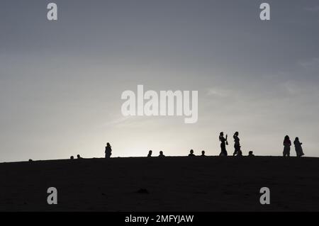 Hinterleuchtete Silhouetten von Menschen auf den roten Sanddünen in Mui Ne Vietnam mit Sonnenuntergang oder Sonnenaufgang dahinter Stockfoto