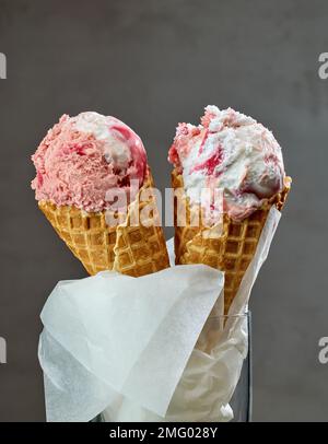 Vanille- und Erdbeereis in Waffelzapfen auf grauem Hintergrund Stockfoto