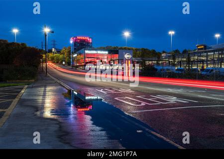 Reflexionen aus dem Auto-Ausstellungsraum im Regenwasser bei Nacht auf der Glasgow Road. Stockfoto