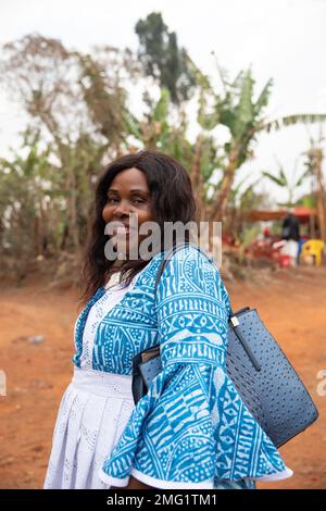 Eine lächelnde afrikanische Frau, gekleidet in traditioneller Kleidung und mit einer Tasche, vertikalem Foto Stockfoto
