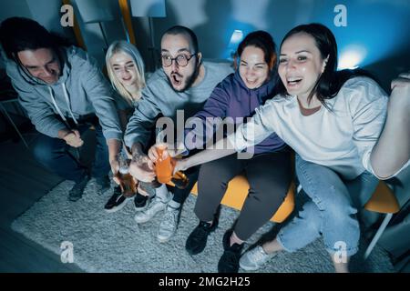 Glückliche Freunde sehen sich zu Hause Fußball oder Fußball im fernsehen an. Feiern mit Flaschen Bier Siegesziel. Stockfoto
