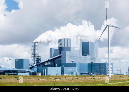 Blick auf ein Kohlekraftwerk mit Biomen, umgeben von Windturbinen an einem bewölkten Sommertag Stockfoto