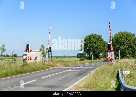 Bahnübergang mit angehobenen Barrieren, damit der Verkehr an einem klaren Sommertag sicher auf dem Land überquert werden kann Stockfoto