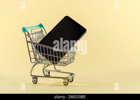 Smartphone in einem kleinen Warenkorb mit hellgelbem Hintergrund. Online-Shopping-Konzept. Kopierbereich. Stockfoto