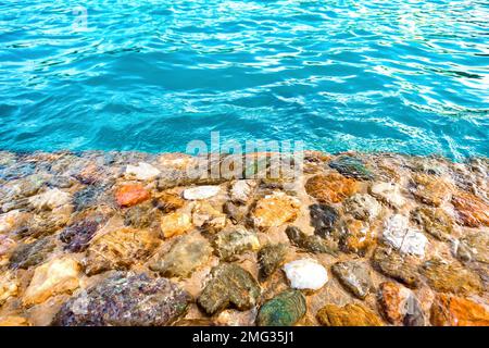 Das Ufer der wunderschönen mehrfarbigen Steine, gewaschen mit klarem blauem Wasser. Hintergrund. Stockfoto