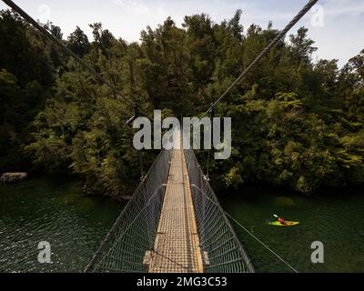 Schwingende Seilbahn-Fußbrücke, die sich über den Süßwasserstrom des Flusses erstreckt, mit Person im Kajak im Abel Tasman National Park South Island New Zealan Stockfoto