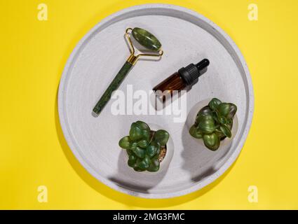 Handmassagegerät für das Gesicht und braune Glasflasche mit Pipette auf runder Platte, Draufsicht Stockfoto