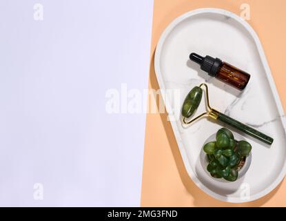 Handmassagegerät für das Gesicht und braune Glasflasche mit Tropfen auf Marmorplatte, Draufsicht Stockfoto