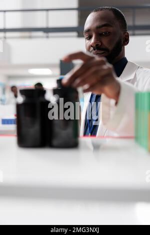 afroamerikanischer Apotheker nimmt Medikamentenflaschen aus dem Apothekenregal, selektiver Fokus auf den Menschen. Apotheke, Sanitäter, Pillen aus der Nähe, Vitamine verkaufen, Apotheken, Vorderansicht Stockfoto