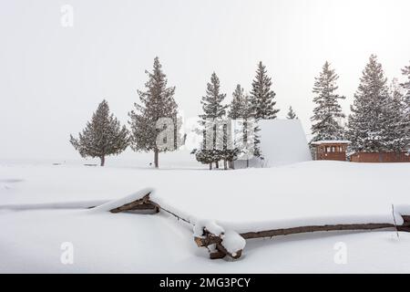 Eine A-Frame-Struktur auf der Insel MANITOULIN (Ontario, Kanada) mit einem Vordergrundzaun mit geteilten Schienen, der fast vollständig von Schnee bedeckt ist. Stockfoto