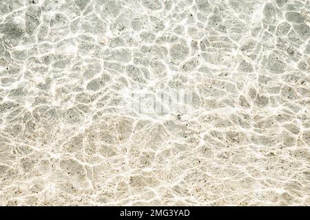 Struktur von Sand, Kieseln und clearwater. Wunderschöner Hintergrund, Draufsicht. Die Sonnenstrahlen scheinen auf dem Wasser. Stockfoto