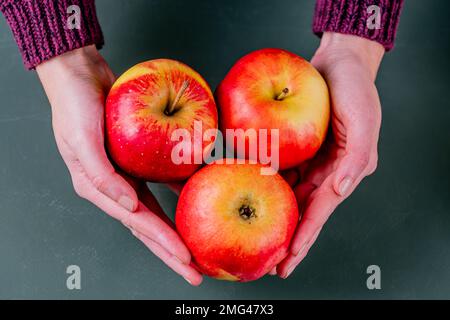 Drei frische rote Äpfel in Frauenhänden. Grüner Hintergrund. Stockfoto