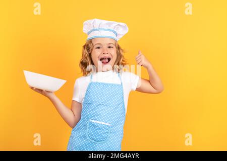 Lustiger Kinderkoch mit Küchenteller, Studioporträt. Kochkinder. Koch-Junge, der gesundes Essen macht. Porträt eines kleinen Kindes im Chefhut Stockfoto