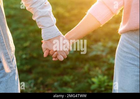 Nahaufnahme der Hände eines Mannes und einer Frau, die die Nationalität eines Weißen kennen und sich beim Spaziergang bei Sonnenuntergang zärtlich gegenseitig festhalten. Zärtlichkeit und romantische Gefühle Stockfoto