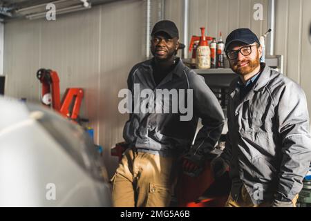 Mittellange Aufnahme von schwarz-weißen Mechanikern, die für ein Bild posieren und lächeln. Werkstattkonzept. Hochwertiges Foto Stockfoto