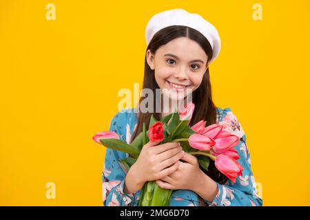 Hübsches, lächelndes, trendiges Teenager-Mädchen mit einem Strauß Tulpen auf gelbem Studiohintergrund. Ein Mädchen genießt Blumen. Stockfoto