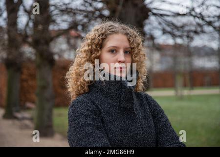 Porträt eines jungen Mädchens mit Locken in einem öffentlichen Park an einem Wintertag Stockfoto