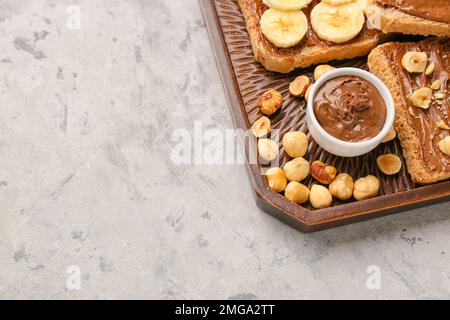 Holzbrett mit leckeren Toasts mit Haselnussbutter, Banane und Nüssen auf hellem Hintergrund Stockfoto