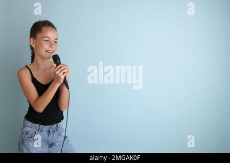 Porträt eines süßen Teenagers, das mit dem Mikrofon singt. Teenager-Mädchen in schwarzem T-Shirt auf isoliertem blauem Hintergrund. Stockfoto