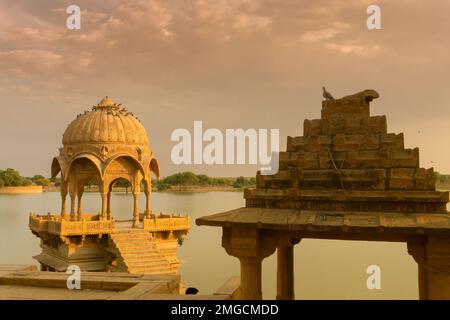 Chhatris und Schreine der hinduistischen Götter und Göttinnen am Gadisar-See, Jaisalmer, Rajasthan, Indien. Indo-islamische Architektur, Sonnenuntergang und bunte Wolken Stockfoto