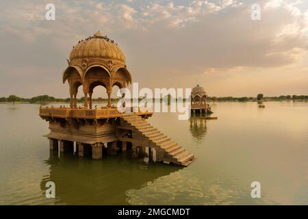 Chhatris und Schreine der hinduistischen Götter und Göttinnen am Gadisar-See, Jaisalmer, Rajasthan, Indien mit Reflexion über Wasser. Indoislamische Architektur. Stockfoto