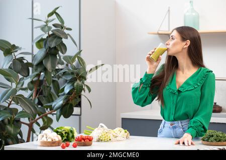 Eine attraktive Brünette trinkt einen grünen Smoothie in ihrer Küche. Das Konzept der gesunden Ernährung, Entgiftung. Stockfoto