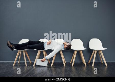 Kann das noch länger warten? Die ganze Länge des Bildes eines gutaussehenden jungen Mannes, der auf einer Reihe von Stühlen lag, während er in der Schlange auf ein Vorstellungsgespräch wartete. Stockfoto