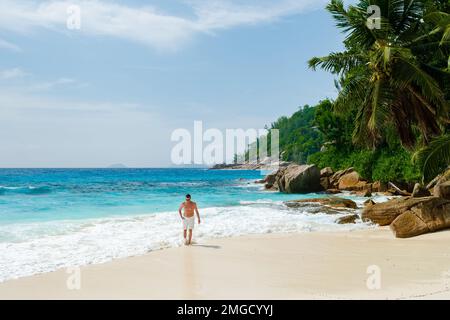 Junge Männer schwimmen kurz an einem weißen tropischen Strand mit Palmen Petite Anse Beach Mahe Tropical Seychelles Islands. Stockfoto