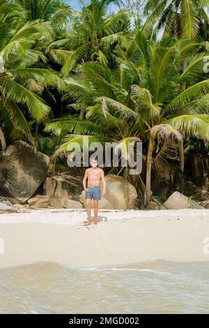 Junge Männer schwimmen kurz an einem weißen tropischen Strand mit Palmen Petite Anse Beach Mahe Tropical Seychelles Islands. Stockfoto