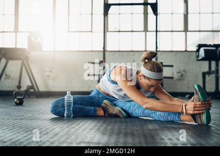 Dehnübungen motivieren ihre Fitness. Eine attraktive junge Frau, die sich in einem Fitnessstudio dehnt. Stockfoto