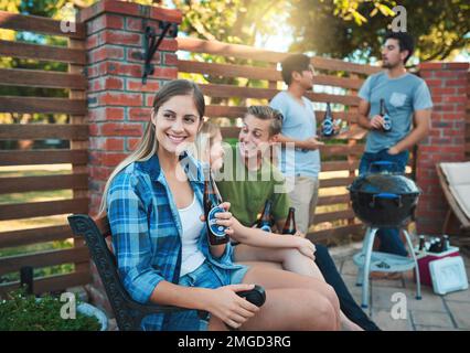 Nichts ist besser als ein Barbecue mit Freunden. Eine glückliche junge Frau, die ein Bier beim Barbecue mit ihren Freunden genießt. Stockfoto
