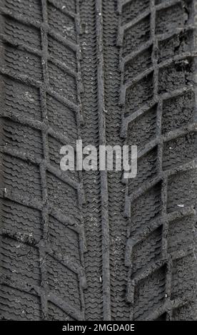 Spuren von Reifenprofilen im Boden. Muster. Dunkler abstrakter Hintergrund. Aufdruck der Räder. Strukturierter Boden. Reifen zeichnen. Stockfoto