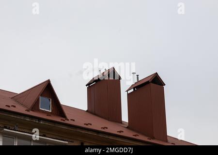 Das Dach des Hauses besteht aus roten Metallfliesen, einem wunderschönen großen Kamin. Stockfoto