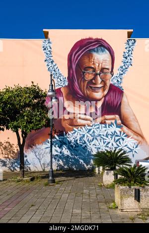 Große kunstvoll bemalte Graffität einer alten Dame, die Blumen an einer Hauswand in der Stadt Milazzo flechtete. Stockfoto