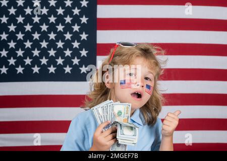 Das amerikanische Dollar-Geld-Banknotenkonzept. Ein Kind, das Geld spart. Kind mit amerikanischer Flagge. Gedenktag. Lustige Kinder mit amerikanischer Flagge auf der Wange. Stockfoto