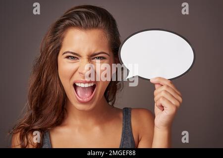 Es reicht, damit ich schreien will. Studiofoto einer attraktiven jungen Frau, die eine leere Sprechblase hält und vor grauem Hintergrund schreit. Stockfoto
