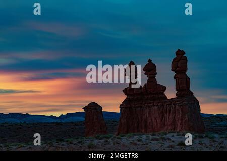 Yjhe Sonnen liegen hinter der Formation Three Sisters im Goblin Valley State Park, Emery County, Utah Stockfoto